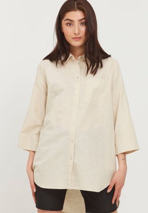 Beige skjorte med knapper lavet af letvægtsstof, med lange ærmer, en brystlomme og en buet kant for en afslappet pasform.