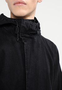 Černá džínová bunda s vysokým límcem a stažitelnou kapucí. Obsahuje přední zip a minimalistický design.
