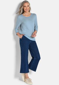 Hellblauer gestreifter Pullover mit Rundhalsausschnitt, kombiniert mit dunkelblauen weit geschnittenen Jeans und beigen Sneakers, die legere Kleidung präsentieren.