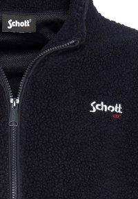 Schwarze Fleece-Jacke mit Reißverschluss und hohem Kragen, aus strukturiertem Stoff, mit weiß-rotem gesticktem "Schott"-Logo.