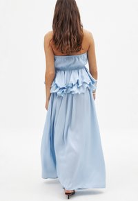 Robe maxi sans bretelles de couleur bleu clair, avec une taille froncée, une jupe fluide et une texture lisse. Présente un corsage ajusté et des couches évasées.