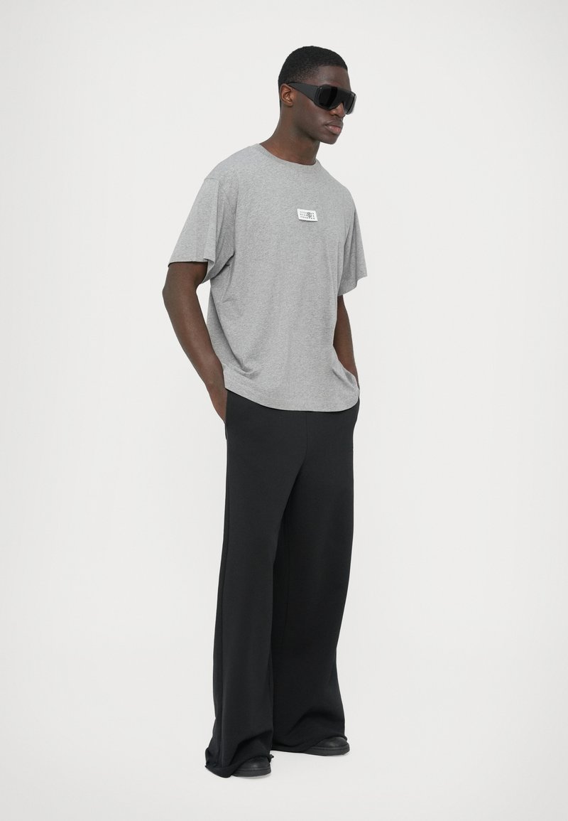 Gray oversized t-shirt with a graphic label, paired with wide black pants. Smooth fabric, relaxed fit, and minimalistic design.