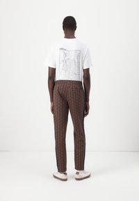 Vit T-shirt med ett grafiskt tryck på baksidan, matchad med bruna mönstrade byxor och vita sneakers med beige detaljer.