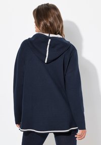 Marineblauer Kapuzenpullover mit kontrastierenden weißen Akzenten, weicher Textur und lässigem Schnitt. Verfügt über lange Ärmel und einen gespaltenen Saum am Boden.