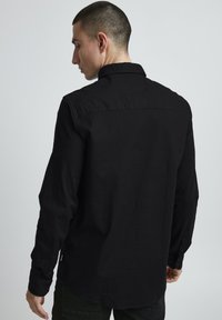 Black long-sleeve shirt made of smooth fabric, featuring a collared neck, buttoned cuffs, and a subtle curved hem.