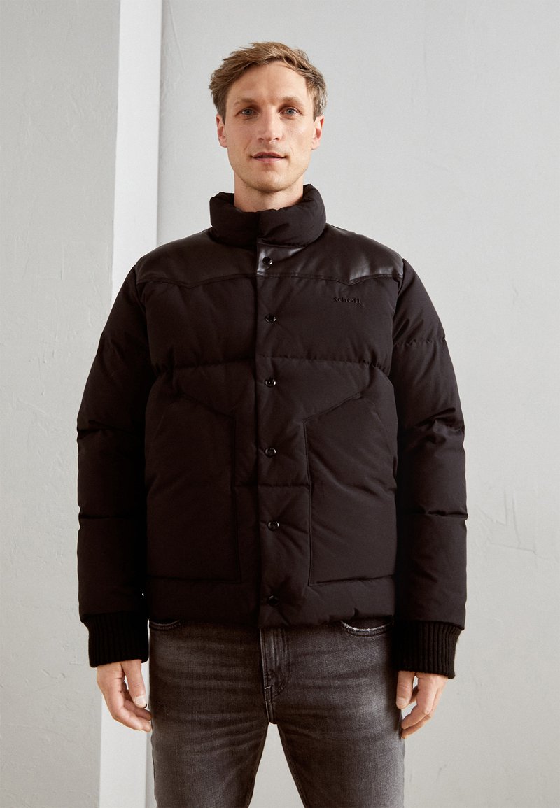 Giubbotto imbottito nero con colletto alto, bottoni a pressione e polsini a costine. Presenta sezioni imbottite e un design del pannello spalla liscio.