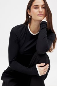 Svart långärmad tröja med vit kant vid kragen och cuffs. Slätt tyg, figursydd design och rundad halsringning. Modell sitter, mjukt belyst.