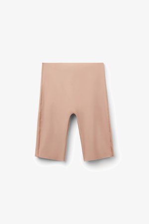 Pantalones cortos ajustados beige hasta la rodilla, hechos de tela elástica suave, colocados planos sobre un fondo blanco.