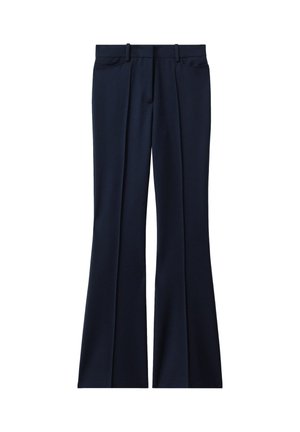 Primer plano de una persona con pantalones y chaqueta a medida de color azul marino oscuro, con una mano ajustando la chaqueta cerca de la cintura.