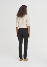Suéter beige de punto con mangas 3/4, combinado con jeans negros ajustados y zapatos slip-on beige, visto desde atrás.