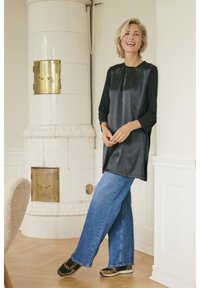 Tunique en satin noir avec un col rond, manches trois-quarts, associée à un jean en denim bleu à jambes larges. Les chaussures présentent un imprimé léopard.