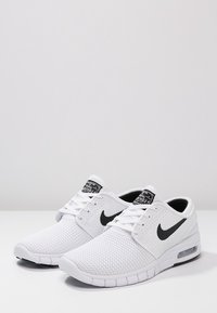 Chaussures de sport blanches en mesh avec un swoosh noir, des lacets plats, un col rembourré et un amorti visible à l'air au talon.