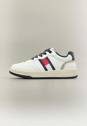 Hvid lavtop sneakers med marineblå snørebånd, marineblå og røde sidelister, beige sål og sort hældetalje på en neutral baggrund.