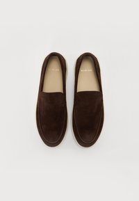 Brune semskede loafers med flad sål, der har et enkelt design, rund tå og subtilt logo-detalje på siden.
