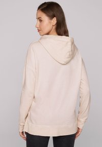 Felpa con cappuccio beige chiaro, maniche lunghe, fessure laterali e vestibilità rilassata. Tessuto morbido con design minimalista e senza motivi visibili.