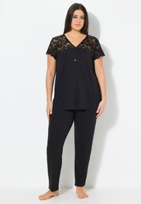 Zwart loungewear-set met een kortemouwen top met kant en knoopdetails, in combinatie met rechte broek. Zachte stofstructuur.