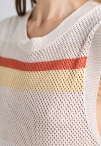 Gros plan d'un top en maille sans manches avec un motif en maille blanche, rayures horizontales rouges et jaunes sur la poitrine.