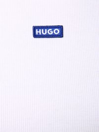 Weißer, gerippter Stoff mit einem blauen rechteckigen aufgestickten Etikett, auf dem das Wort "HUGO" in weißen Buchstaben steht.