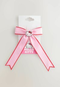 Lyserød satinbånd sløjfe med røde kanter, der har et Hello Kitty emblem i midten, fastgjort til et hvidt kort med en lyserød baggrund.