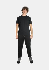 T-shirt nera a maniche corte abbinata a pantaloni felpati neri con una striscia laterale. Il modello indossa sneakers grigie con una parte superiore testurizzata.