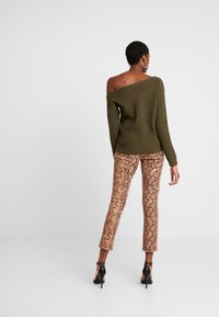 Oliivinvihreä, ribbineulottu olkapäät paljastava neule, yhdistetty ruskeansävyisiin, käärmekuvioisiin tiukkoihin housuihin ja mustiin korkokenkiin.