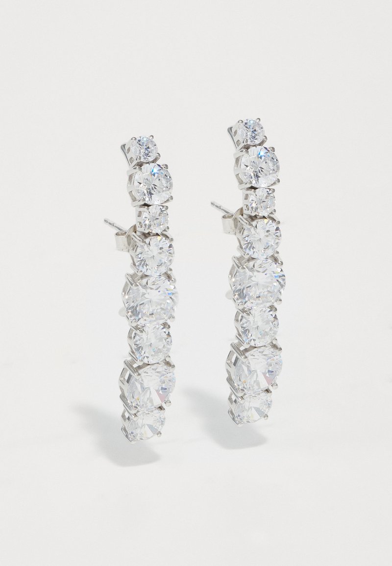 Διαφανή κρυστάλλινα σκουλαρίκια με σχήμα κρίκου και μεταλλική βάση σε ασημί απόχρωση, που διαθέτουν ακολουθία κυκλικών πετρών σε διάφορα μεγέθη.