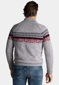Gebreide trui in lichtgrijs met rode, marineblauwe en zwarte patroonaccenten op de rug. Heeft een hoge hals en ribgebreide manchetten.