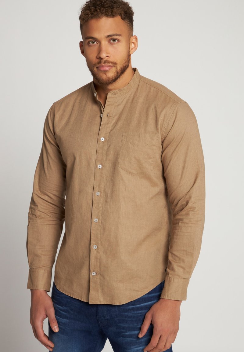 Camisa de manga larga de color marrón claro con cuello abotonado, bolsillo frontal y una tela texturizada. Combinada con pantalones vaqueros de mezclilla azules.