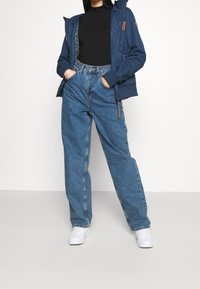 Marinblå huva jacka, svart höghalsskorta och ljusblå vida jeans. Vita sneakers. Jackan har ett blommigt foder och läderdetaljer.