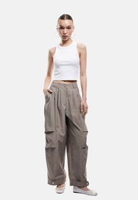 Lys grå oversized bukser med plisséer, sidelommer og knapdetaljer, parret med en hvid ribbet crop top og hvide balletflade sko.