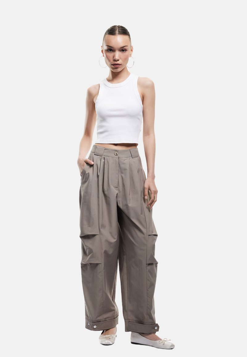 Lys grå oversized bukser med plisséer, sidelommer og knapdetaljer, parret med en hvid ribbet crop top og hvide balletflade sko.