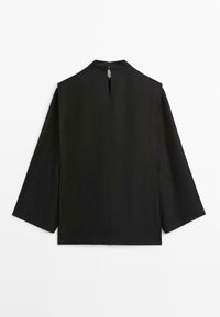 Haut noir à manches longues avec col montant et ouverture en forme de goutte dans le dos, vu de dos sur fond blanc.