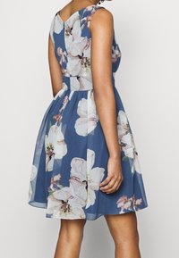 Šaty s květinovým potiskem s přiléhavým korzetem a plnou sukní. Vyrobené z lehké látky v modré barvě, s velkými bílými a růžovými květinovými vzory.