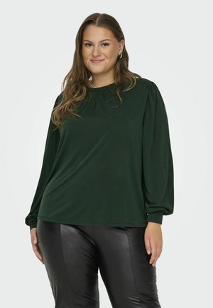 Dunkelgrüner Pullover mit langen, puffigen Ärmeln und rundem Ausschnitt aus weichem Material, kombiniert mit schwarzen, glänzenden Leggings.