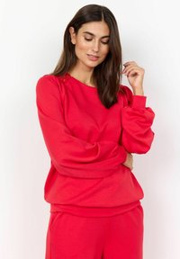 Roter Pullover mit Ballonärmeln, strukturiertem Schulterdetail und gerippten Bündchen. Weicher Stoff mit lässiger Passform.