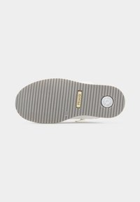 Semelle de chaussure avec des rainures horizontales, un élément circulaire près du talon et l'étiquette "PRIMIGI" au centre sur un fond gris clair.