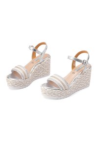 Sandali wedge argento con tomaia intrecciata, dotati di due cinturini metallici e una piattaforma texturizzata. La suola è bianca, aggiungendo contrasto.