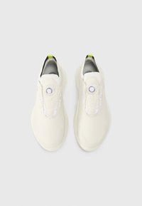 Chaussures de sport légères en blanc cassé, dotées d'un dessus lisse en synthétique, d'un système de laçage rond et d'une semelle texturée avec une touche de vert.