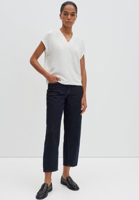 Haut blanc à manches courtes avec un col en V, associé à un jean large bleu foncé et des mocassins noirs. Design simple et texturé sans motifs visibles.