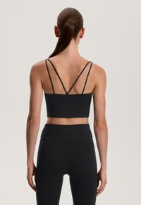 Crni sportski bralet s tankim ukriženim trakama na leđima. Mat površina s minimalnim brendom i krojem koji se dobro prianja uz tijelo. Uparen s visokim tajicama.