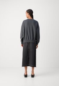 Felpa oversize grigia scura con orlo e polsini a coste, abbinata a una lunga gonna in denim nera con orlo sfrangiato e spacco laterale.