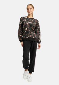 Zwarte bloemen sweatshirt met lange mouwen en ribgebreide manchetten, gecombineerd met zwarte broek en witte sneakers. Het bloemenontwerp bevat roze en beige tinten.