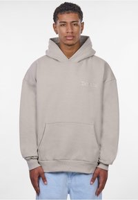 Grauer oversized Hoodie mit einer Fronttasche und Kapuze mit Kordelzug. Mit eingesticktem "Dropsize"-Logo auf der Brust. Weiches Material und Rippbündchen.