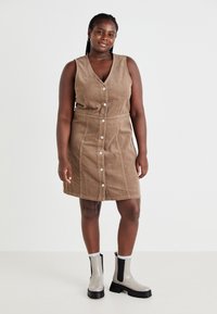 Brown corduroy sleeveless dress with button front, cinched waist, and straight cut. Worn with gray ankle boots featuring black accents.