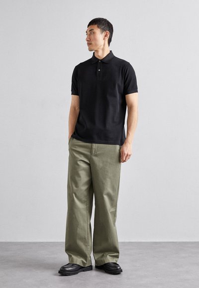 Sort kortærmet polo skjorte med klassisk krave, parret med løstsiddende olivengrønne bukser og sorte klodsede sko. Simple, minimalistisk design.