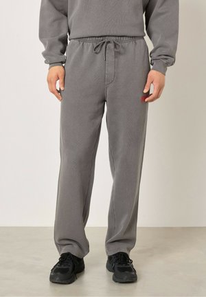 Pantalon de survêtement gris en tissu doux avec une coupe décontractée, une taille élastique, un cordon de serrage et des poches latérales. Chaussures de sport noires portées.