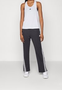 Vit atletisk linne med rund hals och svart logotyp, kombinerat med svarta byxor med vita ränder på sidorna. Vita sneakers.