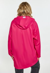 Rózsaszín vízálló dzseki kapucnival, sima tapintású és laza szabású. Figyelemre méltó varrási részlet fut végig a háton.
