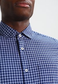 Blå och vit rutig skjorta med knäppbar krage, med vita knappar, en slät yta och en bröstficka.