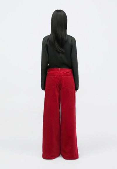 Red corduroy wide-leg pants with a textured finish, high waist, and back pockets. Paired with a black long-sleeve top.